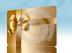 A gold gift card with a gold bow and ribbon is pictured here isolated on the background