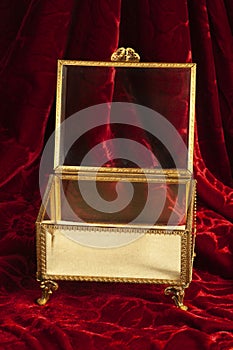 Gold and glass jewelry box with feet sits open on rich red velvet.