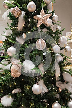 Gold glitter baubles hanging on an artificial festive Christmas tree wrapped with gold stars