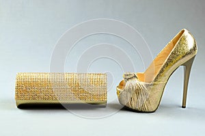 Gold high-heeled shoe and clutch bag on a gray background