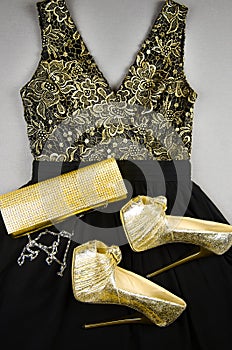 Gold high-heeled shoes, clutch bag and black dress with gold accentson
