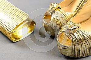 Gold high-heeled shoes and clutch bag on a gray background
