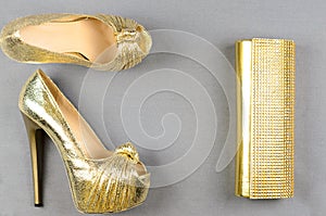 Gold high-heeled shoes and a clutch bag on a gray background