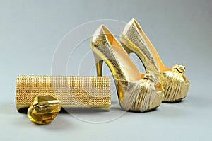 Gold high-heeled shoes, clutch bag and perfume on a gray backgr