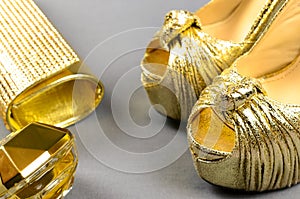 Gold high-heeled shoes, clutch bag and perfume on a gray backgr