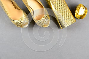 Gold high-heeled shoes, clutch bag and perfume on a gray background