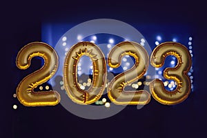 Gold inflatable foil balloons numbers 2023 on the window against the background the night city, in neon light. New year