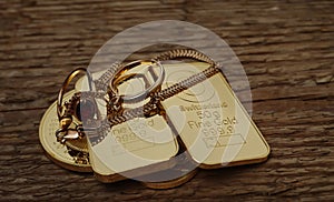 Gold jewelry, gold bars and coins on a wood texture background.
