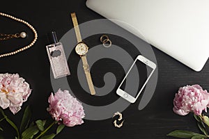 Gold jewelry, phone and laptop flat lay on black background