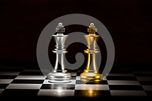 gold king chess facing silver king chess on chess board , business strategy concept
