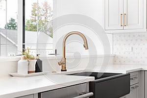 A gold kitchen faucet detail with a black apron on sink.