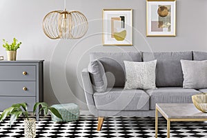 Gold lamp in grey living room interior with poster above grey so