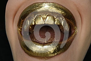 Gold lips. Gold paint from the mouth. Golden lips on woman mouth with make-up.