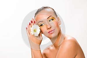 Gold make up. Brown sleek hair beautiful woman with white flower in hands close to face looking down.