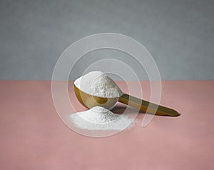 Gold measuring spoon with collagen on pastel pink gray background. Powdered hydrolyzed fish collagen supplement. photo