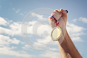 Gold medal held in hand raised against sky background