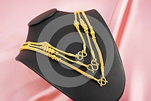 The Gold necklaces in necklace display stand on pink color silk textile