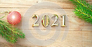 Gold numbers 2021 on a wooden background with Christmas decorations: green branches of spruce, red ball. New Year concept, frame,