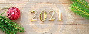 Gold numbers 2021 on a wooden background with Christmas decorations: green branches of spruce, red ball. New Year concept, frame,