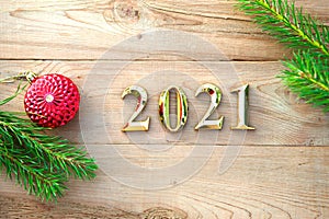 Gold numbers 2021 on a wooden background with Christmas decorations: green branches of spruce, red ball. New Year concept, frame,