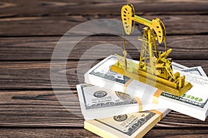 Gold oil pump on wads of money on a wooden background. fuel industry