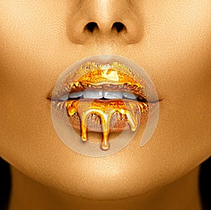 Gold paint drips from the lips, golden liquid drops on beautiful model girl`s mouth, creative abstract makeup