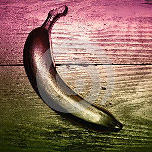 Gold painted banana on golden and wooden background. Double color filter.