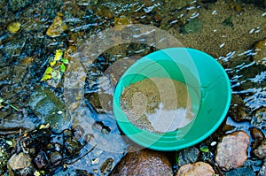 Gold panning goldpan filled with mineral rich soil,  in gold bearing stream.  Fun, recreational outdoor activity of prospecting. photo