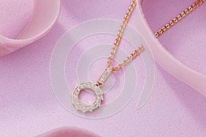 Gold pendant necklace with diamonds on pink background