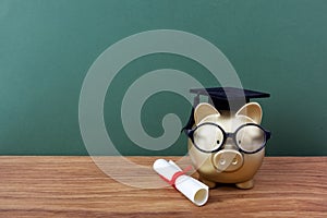 Gold piggy bank with a grad cap and diploma in front of green chalkboard. Education scholarship