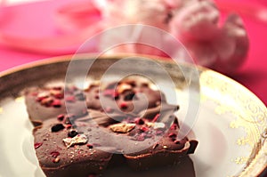 Gold and pink porcelain saucer with artisan chocolate on bright fuchsia pink background with copy space