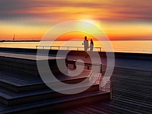 Gold pink sunset at pier summer  sea romantic couple walking relaxing on promenade  wooden tables and bench  on beach Tallinn Esto