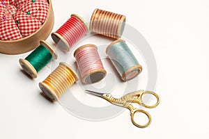 A gold plated stork scissors and colored threads spools on a white background