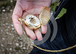 Gold pocket watch with chain open in hand to check time taken outdoor held by man wearing suit on wedding day