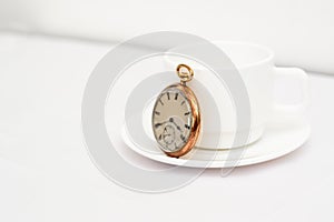 Gold pocket watch on a cup of coffee, all on a white surface