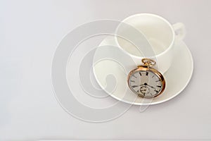 Gold pocket watch on a cup of coffee, all on a white surface