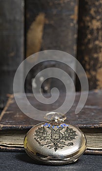 Gold pocket watch Pavel Bure on a gold pendant. Royal Russia. pocket watch on a dark background with books.