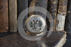 Gold pocket watch Pavel Bure on a gold pendant. Royal Russia. pocket watch on a dark background with books.