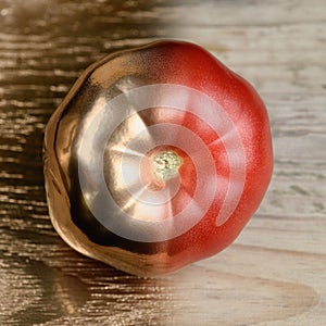 Gold and realy half painted tomato on golden and wooden background.