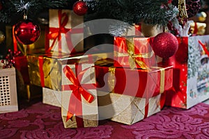 Gold and red gift boxes are under the Christmas tree near the fireplace