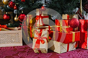 Gold and red gift boxes are under the Christmas tree near the fireplace