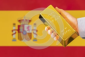 gold reserve of the Spain concept. Gold bar in hand on flag Spain background