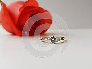 gold ring of engagement with diamond stone, to ask for marriage and a red rose flower in the background