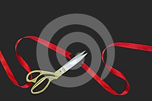 Gold scissors cutting red silk ribbon against black background
