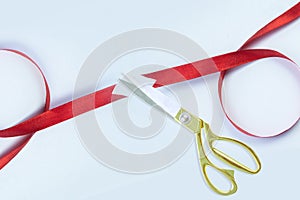 Gold scissors cutting red silk ribbon against white background