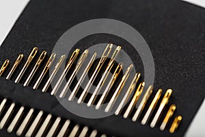 Gold sewing needles on a black background in a row