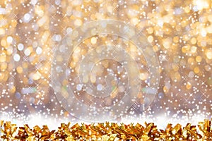 Gold shiny tinsel on background of golden bokeh with snow and copy space.