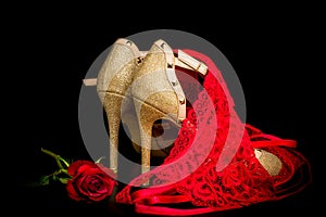 Gold shoes on black background with red rose and red knickers photo