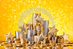 Gold and silver coins stacked with shiny golden stars and glitter bokeh background