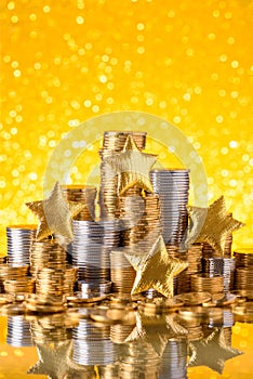 Gold and silver coins stacked with shiny golden stars and glitter bokeh background